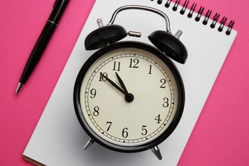 Alarm clock, pen and notebook on pink background, flat lay. Reminder concept
