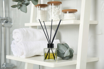 Aromatic reed air freshener, toiletries and rolled towels on white wooden shelf in bathroom