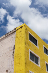 Corner of an old weathered yellow concrete building juxtaposed against a blue sky and cloudscape