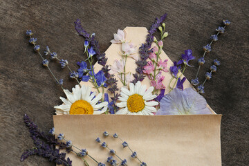 Flat lay composition with beautiful dried flowers in envelope on wooden background