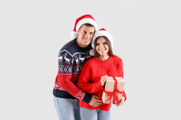 Beautiful happy couple in Santa hats holding Christmas gift on light background