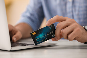 Man using laptop and credit card for online payment at table indoors, closeup