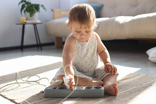 Baby girl playing with charger and power strip on floor at home. Dangerous situation