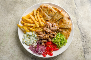 Gyros on plate with chicken, french fries,vegetables and greek sauce top view on stone table