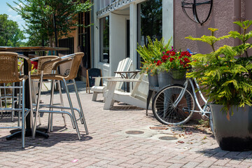 A courtyard garden outside a bakery shop with multiple wooden chairs, tables and bar stools....