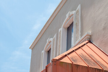 Two long glass windows with curved stucco trim over the openings.  The exterior wall is beige textured cement. There's a copper shade cover over a lower level window. The metal is orange in color.  