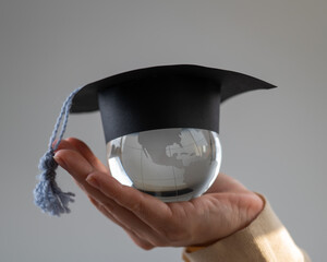 Woman holding a crystal globe wearing a graduation cap. 