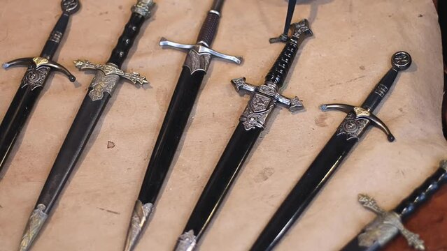 Medieval historical weapons daggers and knives lie on craft paper on a stand for sale, flat lay close-up in slow motion and plano receding motion. Medieval concept art, dagger and knives collection.