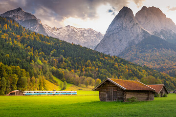 Train in Bavarian alps at autumn and wooden barns at sunset, Garmisch, Germany - obrazy, fototapety, plakaty