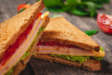 Sandwich with ham, cheese, tomatoes and lettuce leaves on wooden rustic table. Close up