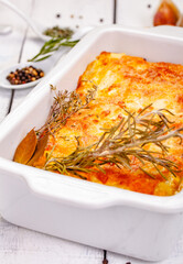 Potato gratin in white casserole dish on wooden rustic table. Close up