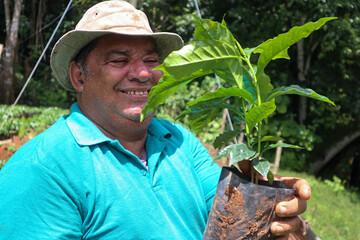 Smiley farmer looking and holding a coffee plant