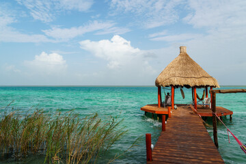 Fototapeta premium Thatched hut at the end of a pier jutting out into the blue water of the Bacalar lagoon