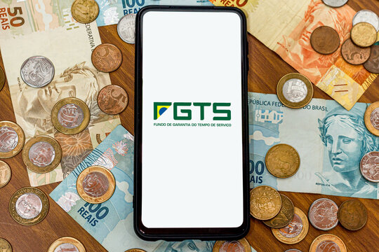 Sao Paulo, Brazil. SEPTEMBER 19, 2022: FGTS logo on smartphone screen with multiple coins and moneys around. FGTS is the Brazilian worker's guarantee fund. Payment by the Brazilian government