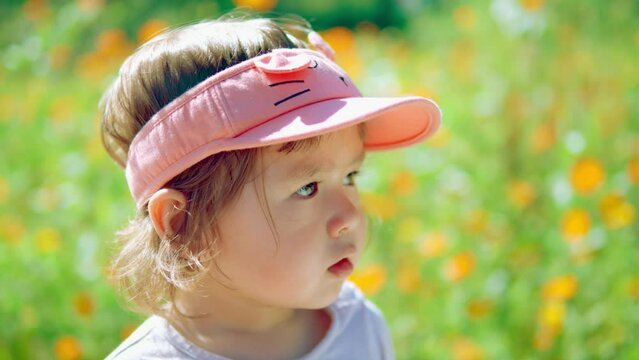 Girl's face close-up looking with caution or wariness at the flowering field on sunny day - slow motion