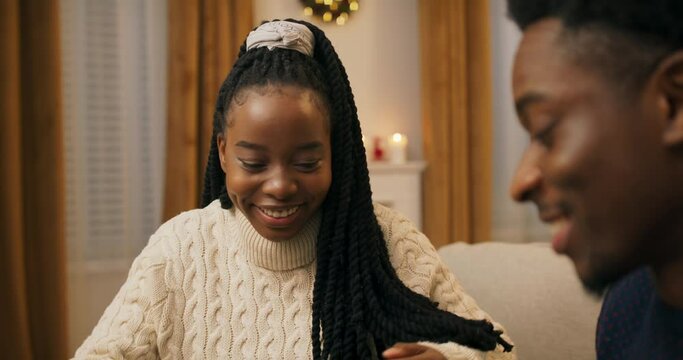 Close-up of two friends of African appearance exchanging gifts. The guy handed the girl gift. She untied the ribbon, opened the box and was pleasantly surprised. Friends are smiling and happy.