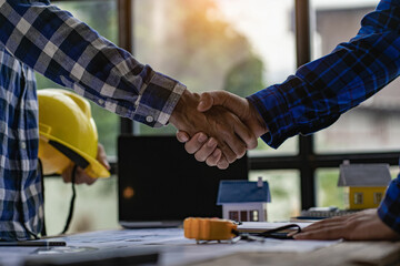 Architects and construction engineers shake hands while working as a team and collaborating ideas after finishing a deal on office blueprints and tabletop house plans.