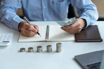 Man calculating money on table with piles of coins and dollars, money saving concept.