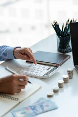 Man calculating money on table with piles of coins and dollars, money saving concept.