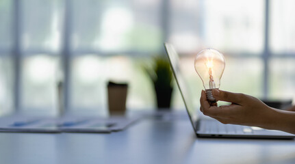 Close-up of a man holding a glowing light bulb with icons of ideas, innovation and business...
