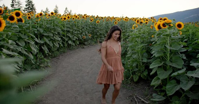 Beautiful joyful girl runs barefoot on dirt road in sunflower field