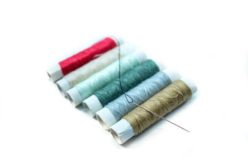 Rows of sewing threads of various colors and sewing needles isolated on white