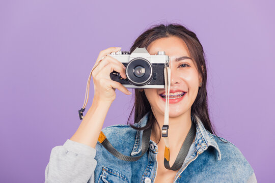 Portrait happy beautiful young woman smile excited wear denims photographer taking a picture and looking viewfinder on vintage photo camera ready to shoot, studio shot isolated on purple background