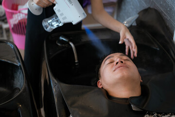 Directly above Asian male lying down for hair wash at hair salon with eyes closed