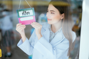 Pharmacist in front of a shop with an "open" sign in Thailand. looking out the glass window