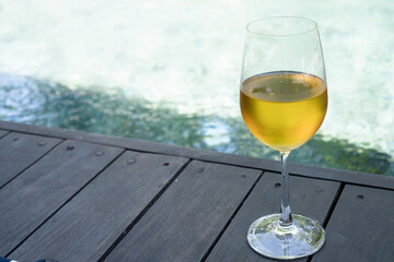 Glass of white wine near a swimming pool in morning of summer. .