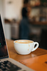Coffee mug with coffee stain near by laptop on wooden table inside the cafe. 