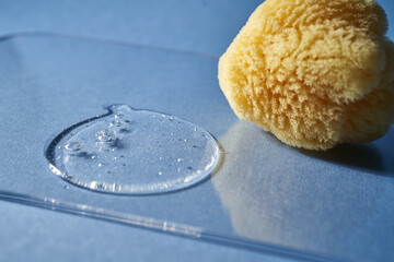 A natural sponge and a drop of gel or shampoo on a blue background.