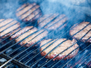 Grilling meat cutlets for burgers. Fast food or street food. Steel grill grate, cutlet in the smoke. Selected focus, macro close-up