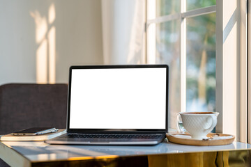 Mockup of laptop computer with empty screen with coffee cup and smartphone on table beside the window of the coffee shop background,White screen