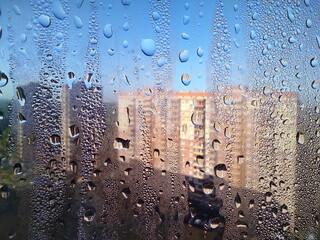 Large drops of rain on the window glass of the house. Residential buildings of a large complex through glass with water drops. Macro photography of water and glass.