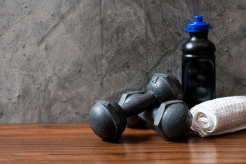 A pair of vintage iron dumbbells with a water bottle and white towel on a wooden floor and a cement...