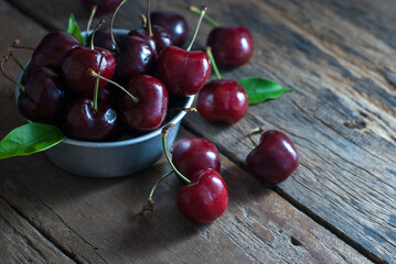 Cherries are placed in the zinc cup and put on a rustic wooden floor, horizontal closeup.