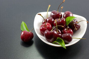 Fresh cherries in a white ceramic bowl and placed on a black background.