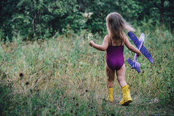 A little girl in a swimsuit with an airplane in her hands in nature, in the sun. Travel concept. Ideas for traveling by plane with a child. Children's imagination: become a pilot, fly an airplane