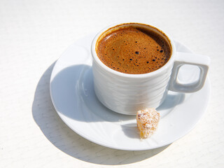 Delicious traditional Turkish Coffee served with Turkish Delight lokum in traditional white ceramic cup on white background in sunny day, close up shot