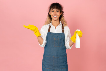 Attractive young Asian woman wearing apron with yellow rubber gloves and holding clean spray on...