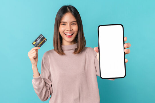 Beautiful Asian woman holding smartphone mockup of blank screen and show credit card on blue background.