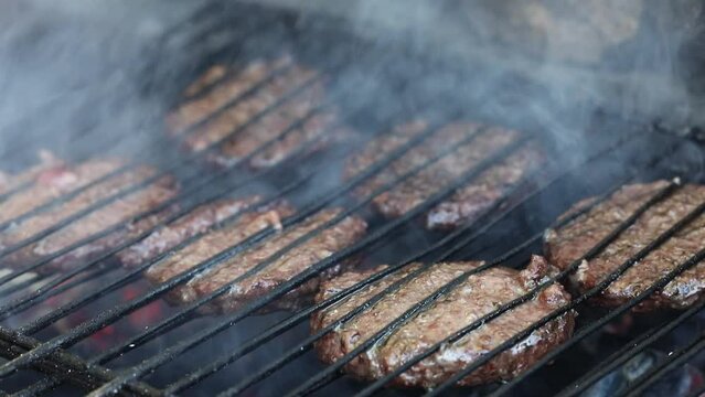 Grilling meat cutlets for burgers. Fast food or street food. Steel grill grate, cutlet in the smoke. Selected focus, macro close-up video footage