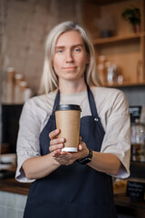 Shot of aged female barman working in coffee shop with blond hairs and coffee cup.