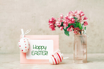 Happy Easter text on card. Easter eggs and spring festive blooming with pink white flowers fruit tree branches in small vase against tender pastel background. Fresh floral background. copy space