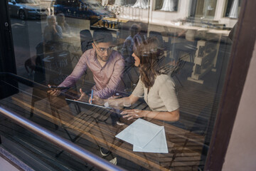 Shot from outdoors through window of two people talking and relaxing in coffee bar.