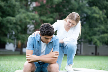 Fototapeta premium Teenager girl consoling sad hispanic boy outdoors in a park. Mourning, depression and anxiety concept.