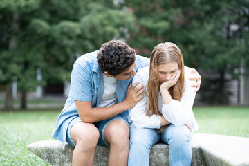 Hispanic boy comforting and hugging sad girfriend outdoors in a park.