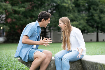Angry and toxic couple shouting each other outdoors in a park. Relationship in adolescence concept.