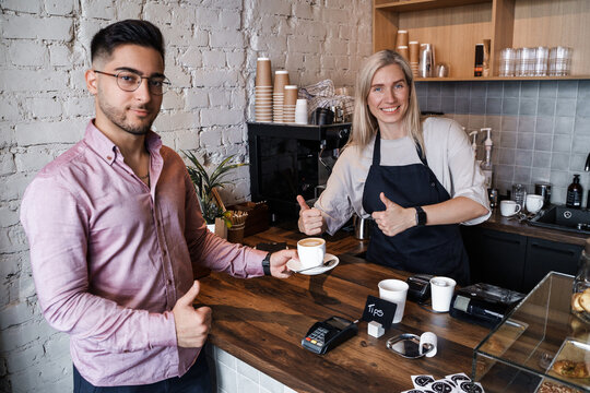 Portrait Of Glad Customer Getting His Coffee Posing Around Counter With Female Barista.